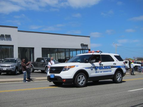 1991 Ford LTD Crown Victoria - white Ford Explorer marked Police City of Cranston with red roof lights drives down a street near a dealership.