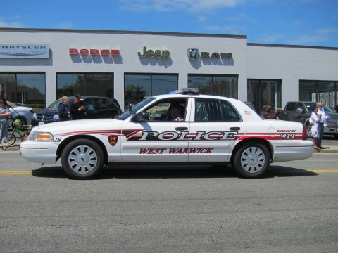 1991 Ford LTD Crown Victoria - white Ford Crown Victoria with red striping marked West Warwick Police sits in front of a Dodge Jeep Ram dealership.