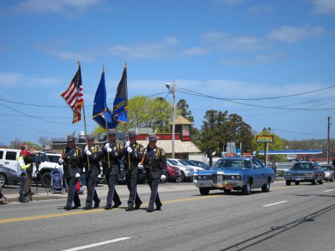 1991 Ford LTD Crown Victoria - uniformed color guard carries flags down a street while a vintage blue police sedan follows behind during a parade.