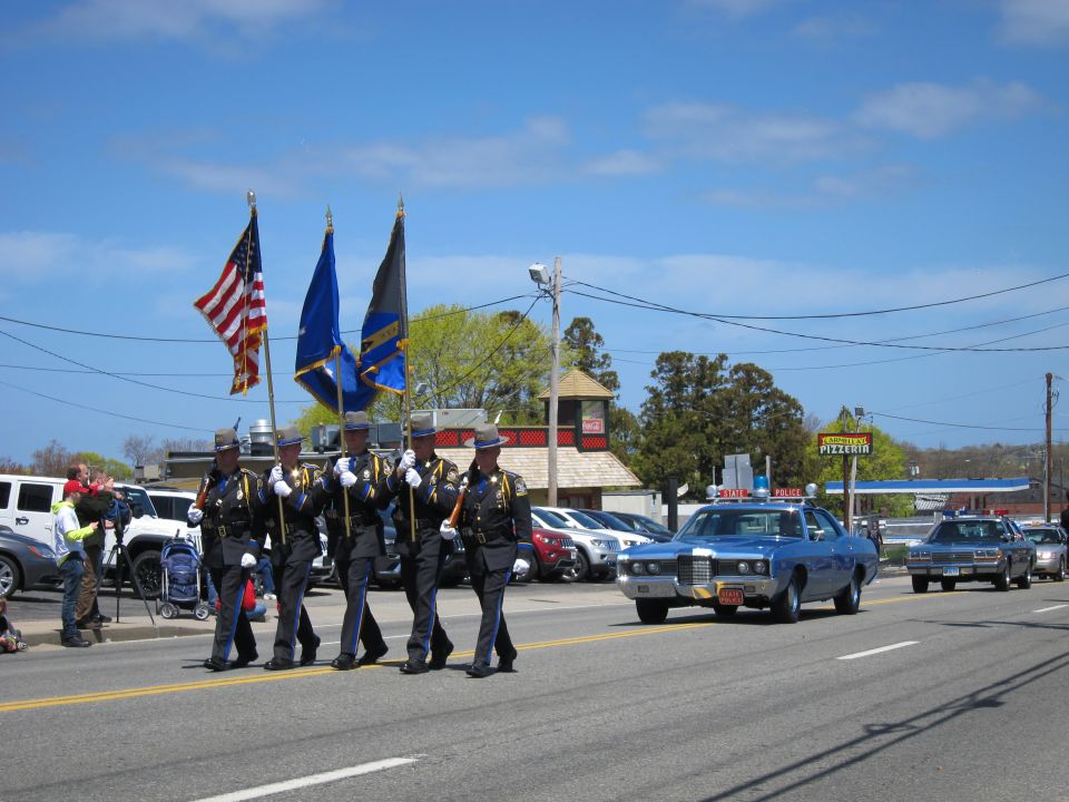 Color guard marching with flags ahead of a blue vintage police car