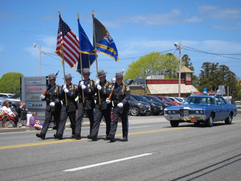 1991 Ford LTD Crown Victoria - uniformed honor guard carries the American and other flags down a street as a blue classic police sedan follows.