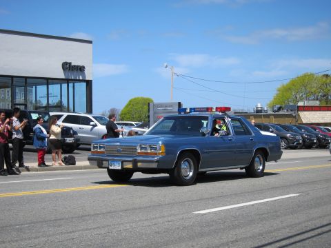1991 Ford LTD Crown Victoria - blue Ford LTD Crown Victoria sedan with roof light bar turns on a street as spectators photograph it.