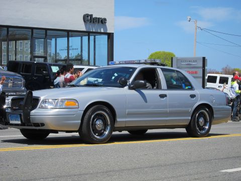 1991 Ford LTD Crown Victoria - silver Ford Crown Victoria with a roof light bar and front push bar drives down a street as people watch.