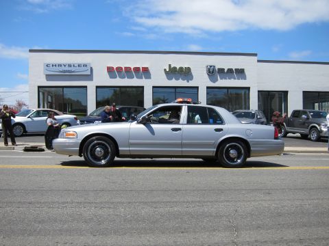 1991 Ford LTD Crown Victoria - silver Ford Crown Victoria with an amber roof light bar sits on a street in front of a Jeep Ram dealership.