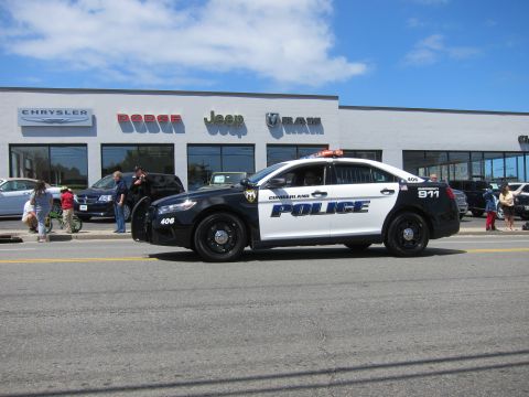1991 Ford LTD Crown Victoria - black and white Ford Taurus marked Cumberland Police number 406 drives past a Chrysler Dodge Jeep Ram dealership.