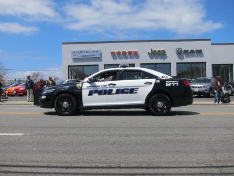 1991 Ford LTD Crown Victoria - black and white Ford Taurus marked Cumberland Police number 406 drives past a Chrysler Dodge Jeep Ram dealership.