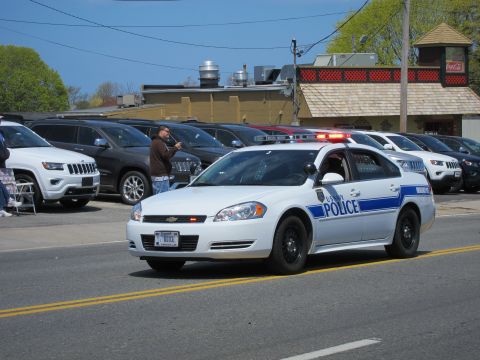 1991 Ford LTD Crown Victoria - white Chevrolet Impala marked Police with red roof lights drives along a street past parked vehicles.