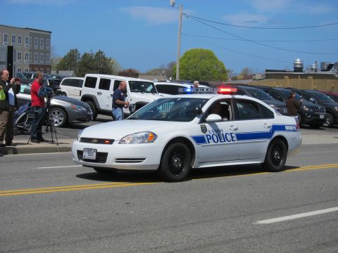 1991 Ford LTD Crown Victoria - white Chevrolet Impala marked Police with a blue stripe and red roof lights drives along a street.