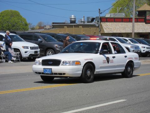 1991 Ford LTD Crown Victoria - white Ford Crown Victoria Capitol Police cruiser with roof lights active passes parked SUVs along a parade route.