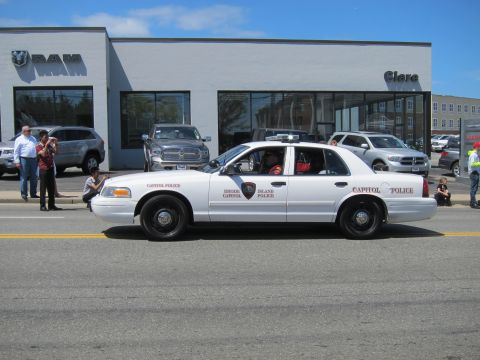 1991 Ford LTD Crown Victoria - white Ford Crown Victoria lettered Rhode Island Capitol Police drives past a RAM auto dealership with spectators.