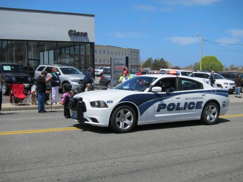 1991 Ford LTD Crown Victoria - white South Kingstown Police Dodge Charger, number 403, passes spectators in front of a dealership building.