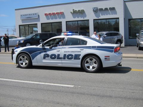 1991 Ford LTD Crown Victoria - white South Kingstown Police Dodge Charger with lights active drives past a Chrysler-Dodge-Jeep-RAM dealership.