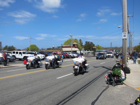 1991 Ford LTD Crown Victoria - Several white police motorcycles ride down a wide street during a parade with spectators and a flag-decked stroller.