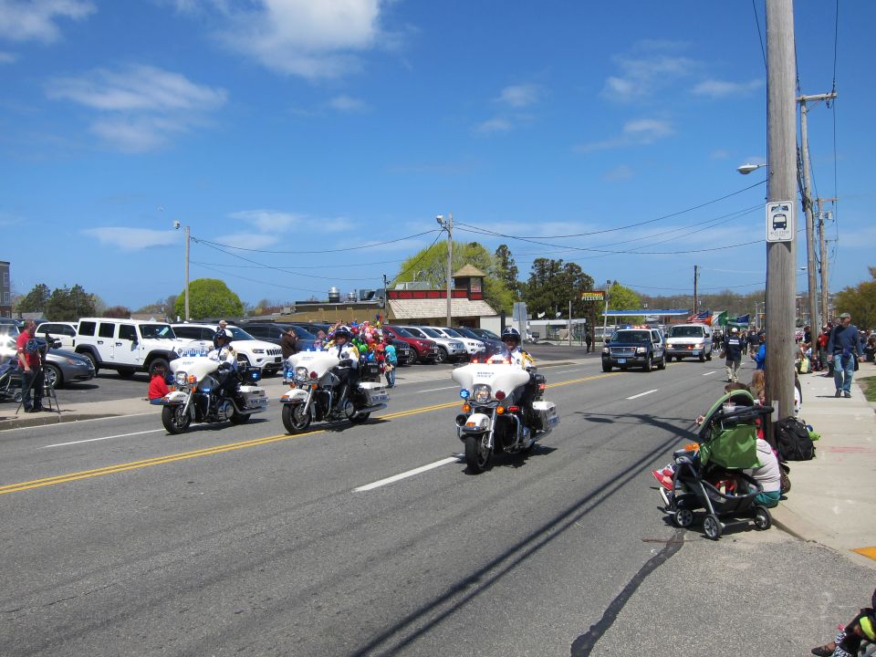 Police motorcycles riding down a street in a parade with crowds and flags