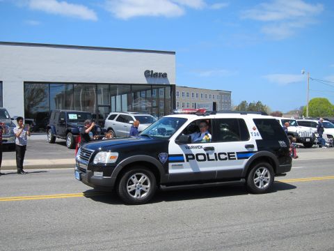 1991 Ford LTD Crown Victoria - black-and-white Warwick Police Ford Explorer SUV drives along a parade route past a dealership and spectators.