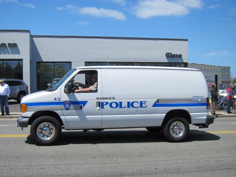 1991 Ford LTD Crown Victoria - white Warwick Police Ford E-Series cargo van with blue striping drives past a dealership in a parade.