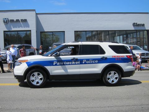 1991 Ford LTD Crown Victoria - white-and-blue Pawtucket Police Ford Explorer SUV drives past a RAM dealership during a parade.