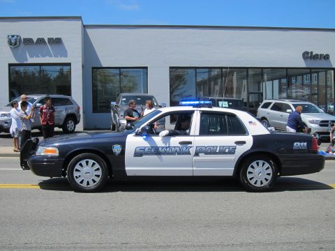 1991 Ford LTD Crown Victoria - black-and-white Seekonk Police Ford Crown Victoria cruiser drives past a dealership with spectators watching.