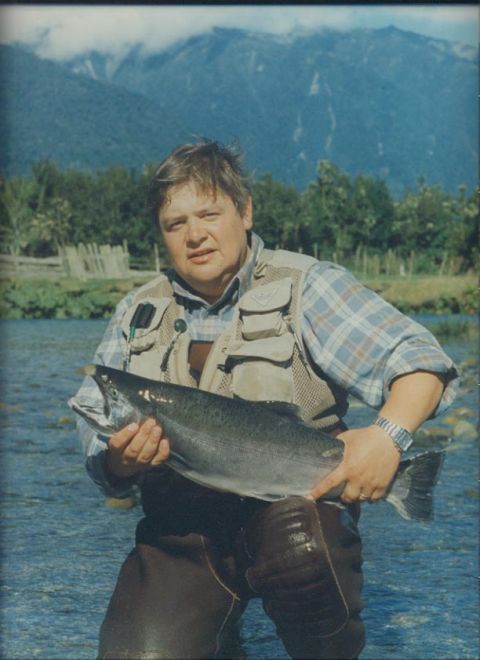 1979 Ford Bronco - A man proudly displays a large salmon he caught while fishing in a river, with a scenic mountain backdrop.