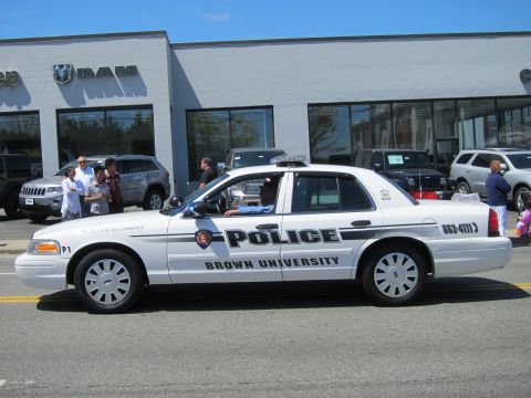 1991 Ford LTD Crown Victoria - white Brown University Police Ford Crown Victoria, unit P1, passes a RAM dealership with spectators on the curb.