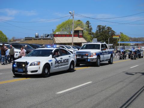 1991 Ford LTD Crown Victoria - white North Providence Police Chevrolet Caprice leads a parade of police vehicles and motorcycles down a sunny street.