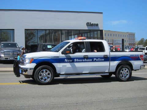 1991 Ford LTD Crown Victoria - white and blue Ford F-150 crew-cab pickup lettered "New Shoreham Police" with roof lightbar drives past a dealership.