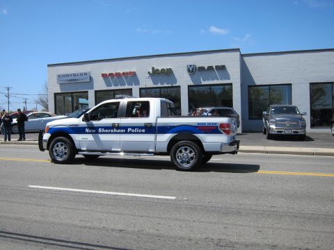 1991 Ford LTD Crown Victoria - white and blue New Shoreham Police Ford F-150 pickup drives along a street in front of a Jeep and Ram dealership.