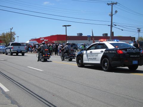 1991 Ford LTD Crown Victoria - black and white police cruiser and two officers on police motorcycles travel down a street lined with spectators.