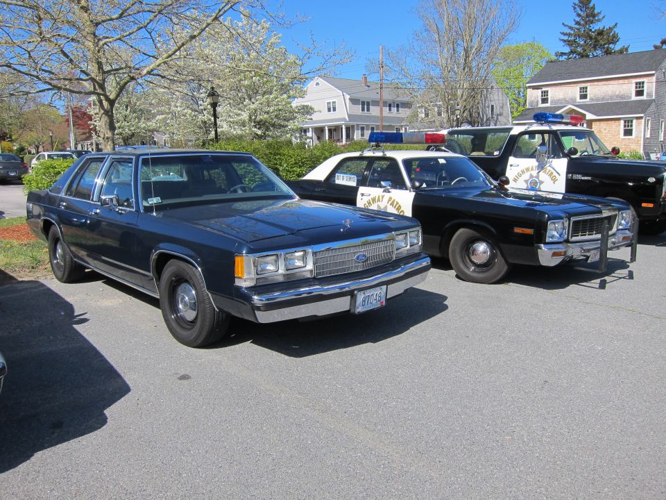 Dark blue Ford LTD Crown Victoria sedan parked beside vintage police cars on a lot