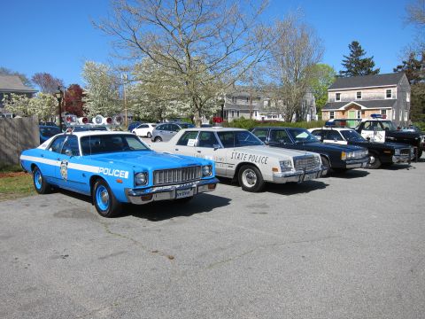 1991 Ford LTD Crown Victoria - light blue vintage Plymouth police sedan leads a row of classic State Police cruisers and a station wagon parked on a lot.