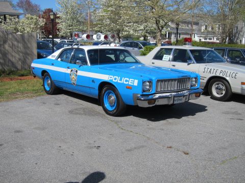 1991 Ford LTD Crown Victoria - light blue vintage Plymouth police sedan lettered "POLICE" with a shield decal parked beside a white State Police cruiser.