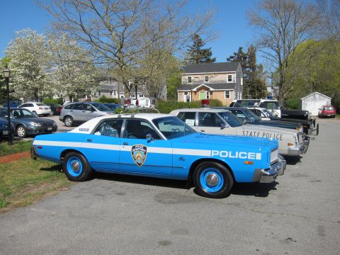 1991 Ford LTD Crown Victoria - light blue vintage Plymouth "POLICE" sedan parked alongside white State Police cruisers on a lot near homes.