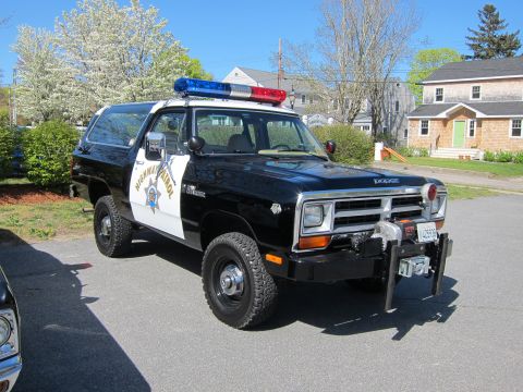 1991 Ford LTD Crown Victoria - black and white Dodge Ramcharger 4x4 with Highway Patrol lettering, roof lightbar and front winch parked in a residential driveway.