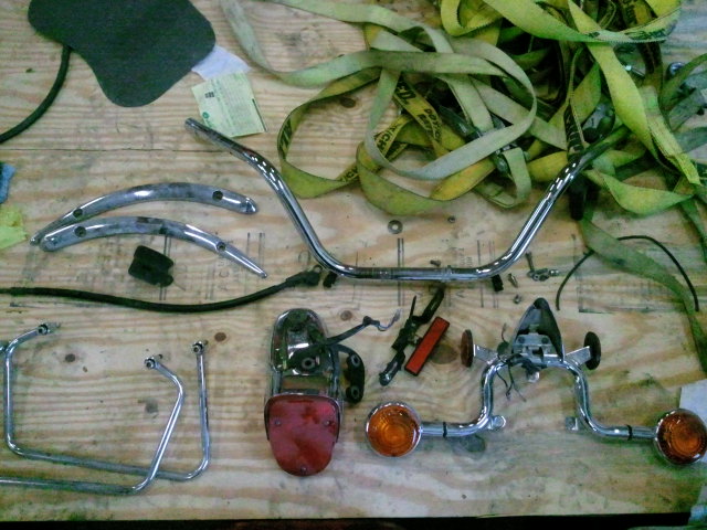 Motorcycle handlebars, taillight, and turn signals laid out on a wooden surface