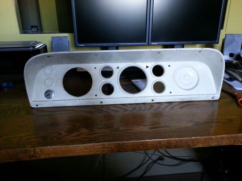 1967 Ford F-100 - Instrument cluster with various circular openings for gauges and a keyhole is placed on a wooden desk.