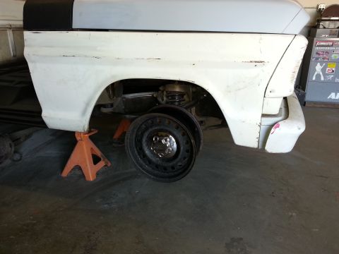 1967 Ford F-100 - The rear fender and cab of a truck are shown on jack stands, with the rear wheel removed for service.