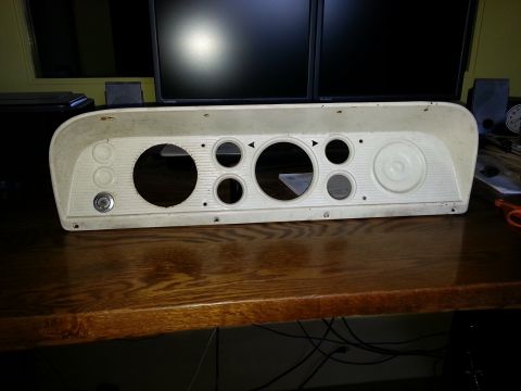 1967 Ford F-100 - A white dashboard instrument cluster with various circular openings for gauges and controls sits on a wooden desk.