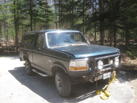 1993 Ford Bronco - This dark green Ford Bronco is shown from a 3/4 front angle, with a brush guard and auxiliary lights mounted on the front.