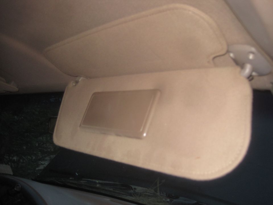 Car's tan sun visor with a mirror is down, showing the interior ceiling and dashboard