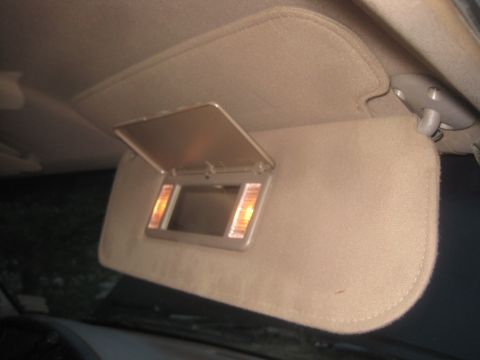 1993 Ford Bronco - The interior of a vehicle shows a tan sun visor with an open vanity mirror and illuminated lights.