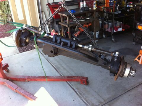 1987 Suzuki Samurai - A front axle assembly is being lifted by chains and straps in a garage setting.