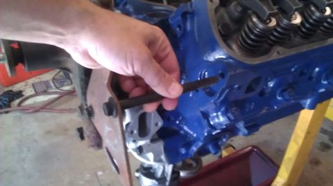 1973 Ford Torino - A hand is shown inserting a bolt into a blue engine block, likely during a repair or assembly process.