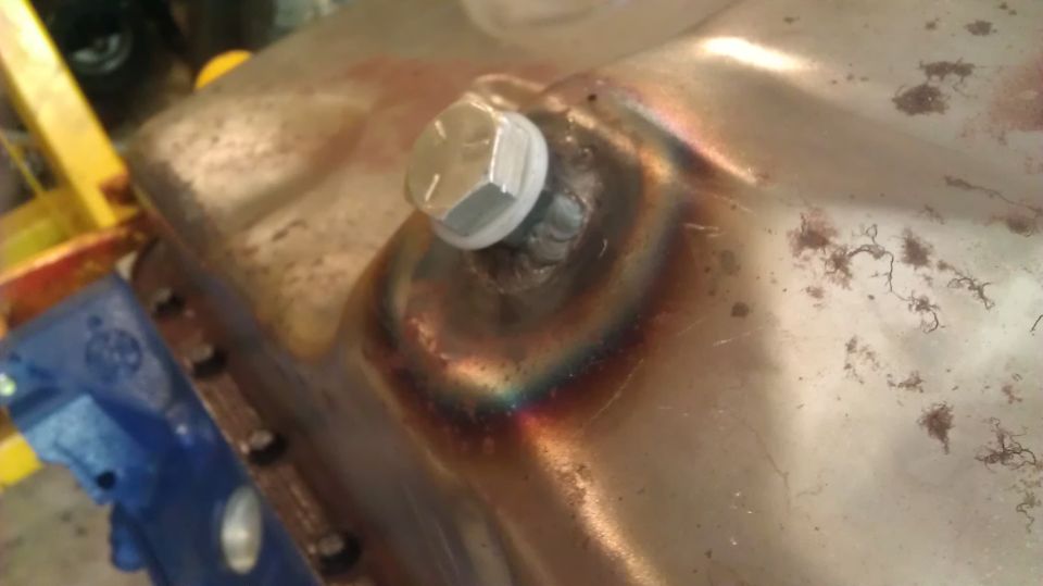 Metal oil pan with a silver hex drain plug and visible weld marks
