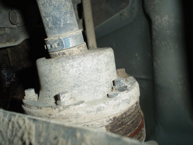 Close-up of a corroded suspension strut mount with hose clamp and mounting bolts