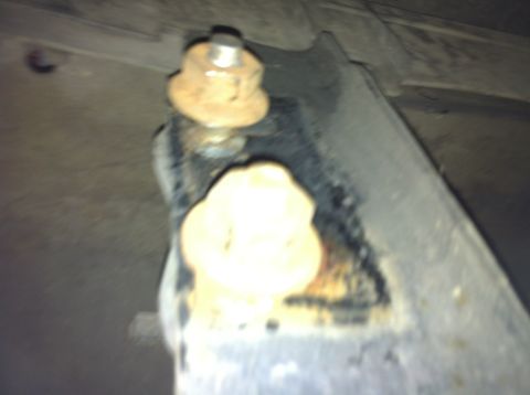 1992 Ford F-150 - A close-up view of a corroded metal bracket with fasteners and a white bushing, likely from a vehicle's undercarriage.