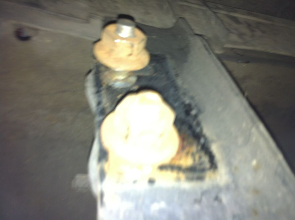Close-up of a rusty metal bracket with two bolts, one on top and one below. A white rubber bushing is visible