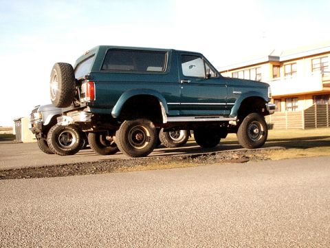 1996 Ford Bronco - Two SUVs are parked side-by-side, one behind the other, with a building in the background.