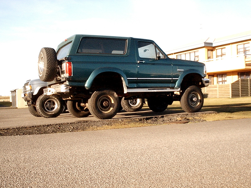 Green two-door Ford Bronco SUV, lifted on large tires, side-rear view