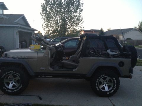 2005 Jeep Wrangler - Side view of a 2005 Jeep Wrangler with its soft top removed, parked outside a garage.