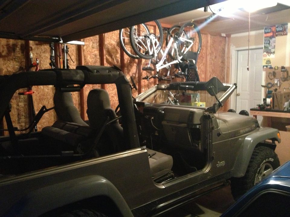 Gray 2005 Jeep Wrangler with doors removed, parked in a garage with bicycles overhead
